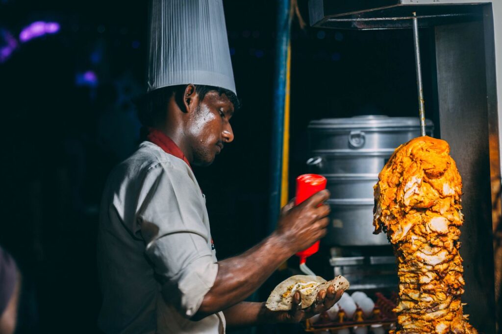 A chef skillfully prepares shawarma in a night market setting, highlighting culinary artistry and street food culture.