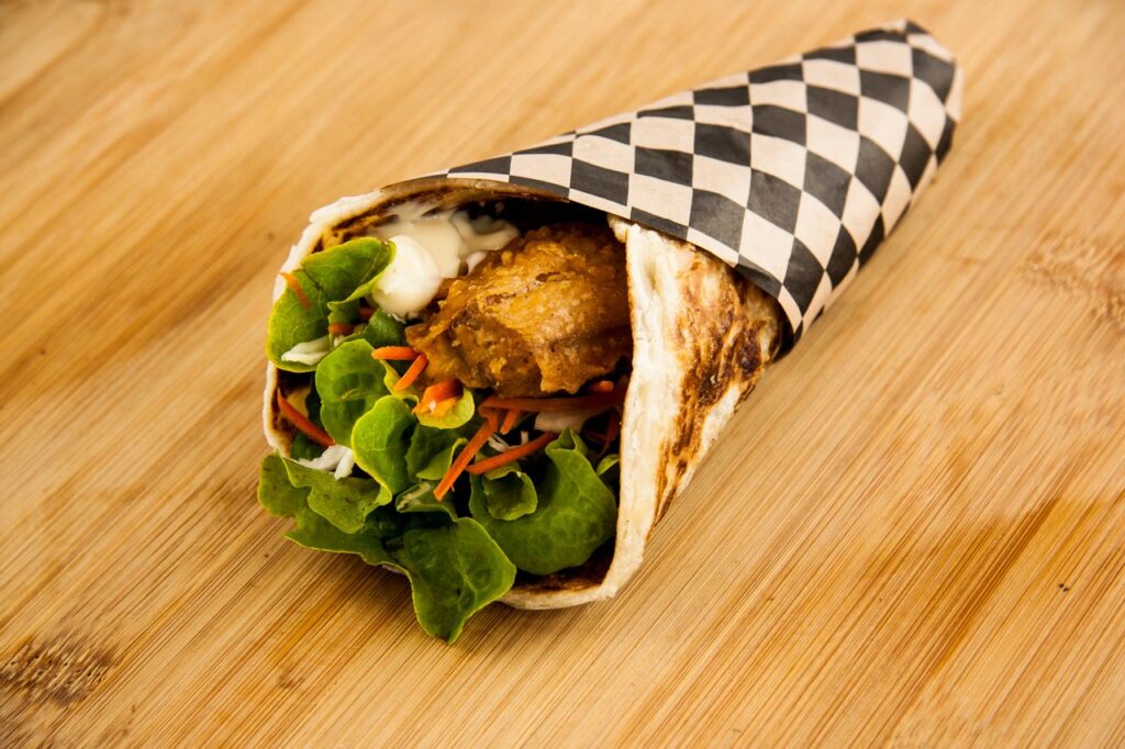 Appetizing shawarma wrap with fresh lettuce and carrots on a wooden background.